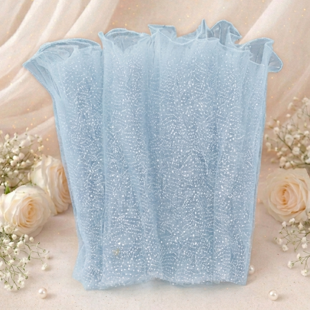 Light blue lace top with ruffled sleeves on a soft pink background with flowers.


